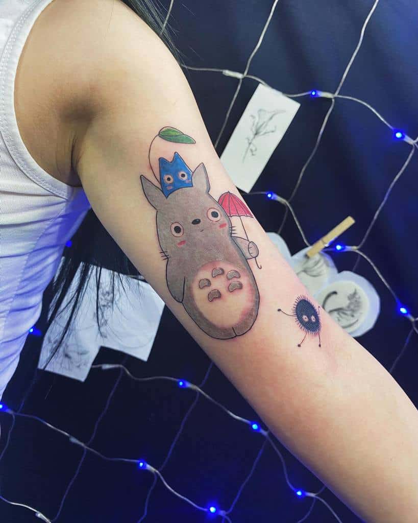 Colorful Totoro tattoo on the inner arm, featuring Totoro with a small umbrella, leaf, and a soot sprite companion nearby