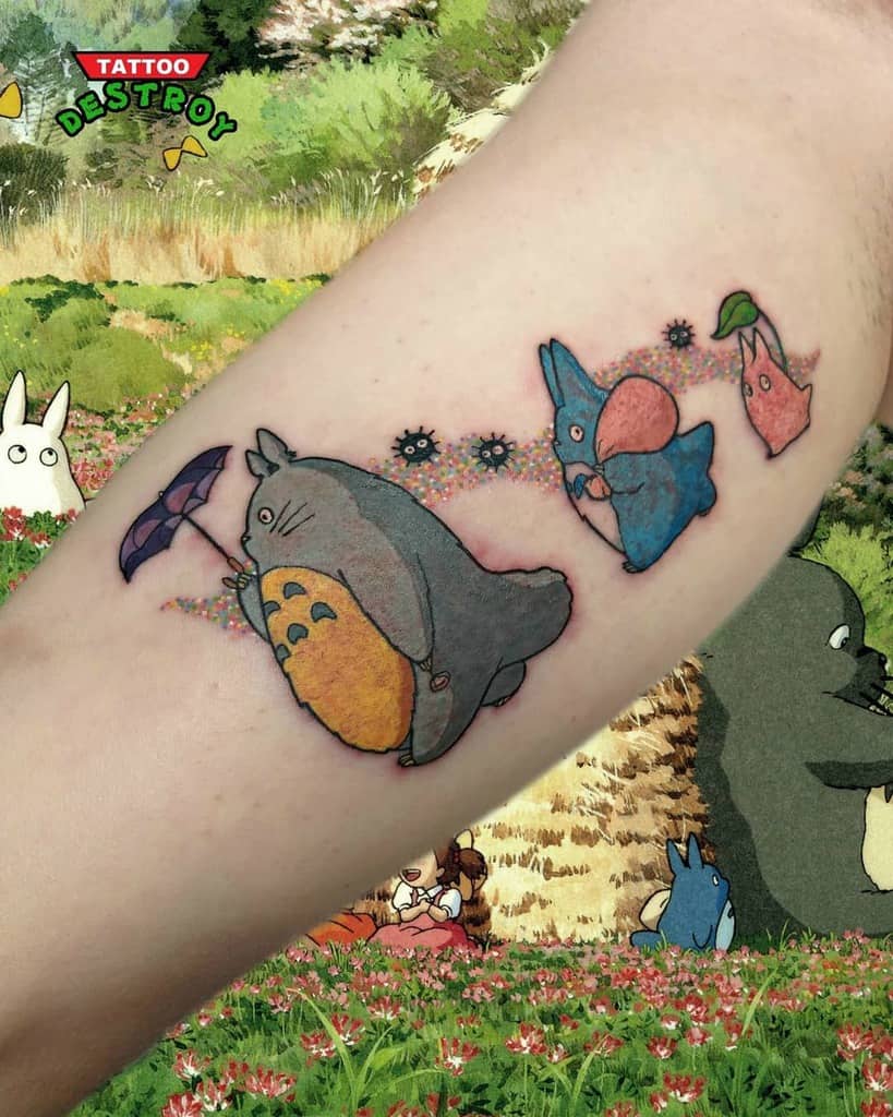 Playful Totoro tattoo on the forearm, featuring Totoro with an umbrella, followed by smaller companions and colorful soot sprites