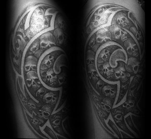 Intricate tribal skull tattoo on upper arm, featuring a spiral pattern filled with small skulls and bold black linework.
