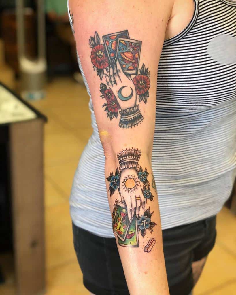 Colorful tarot-inspired tattoo with a mystical hand, crescent moon, sun, floral accents, and vibrant card details
