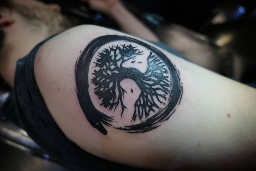 Black ink tree of life tattoo with roots and branches forming a yin-yang circle, symbolizing balance and connection