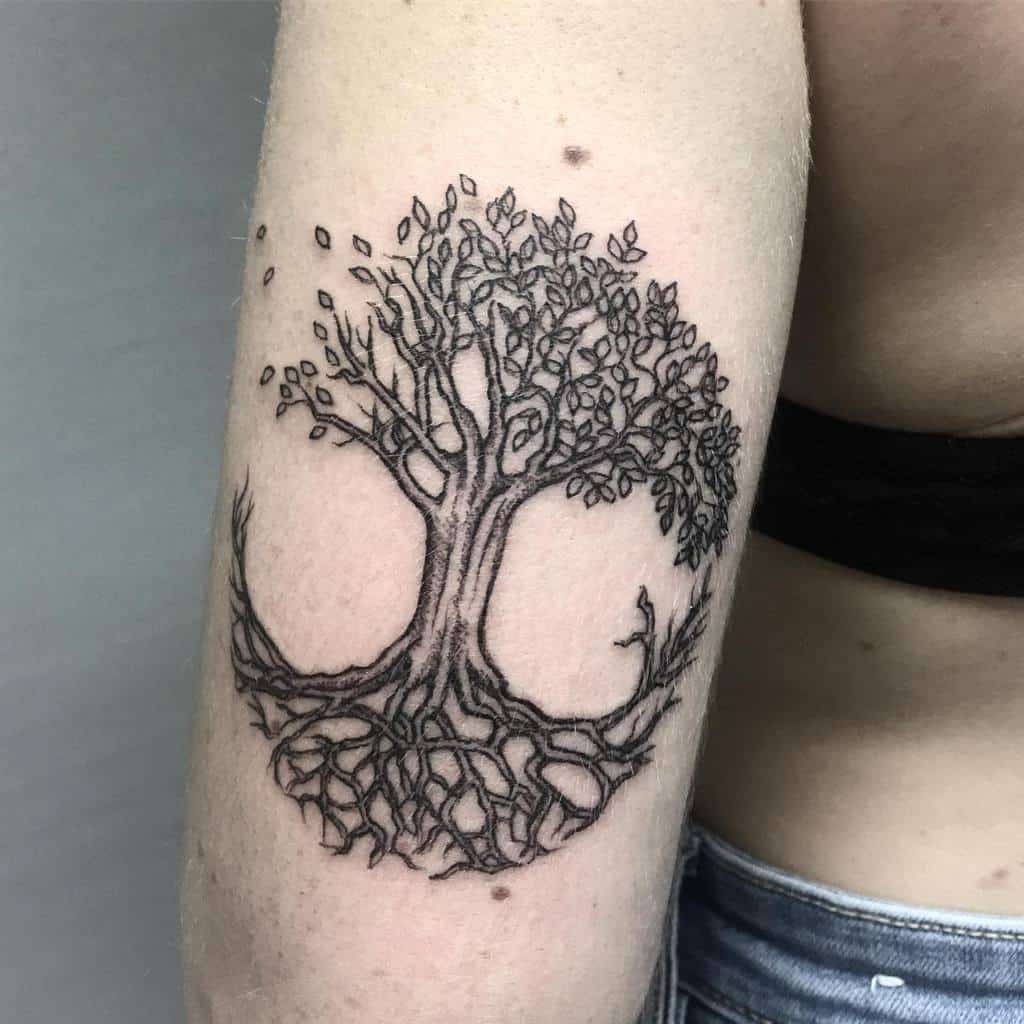 Minimalist tree of life tattoo with detailed roots and branches forming a circular balance on the upper arm