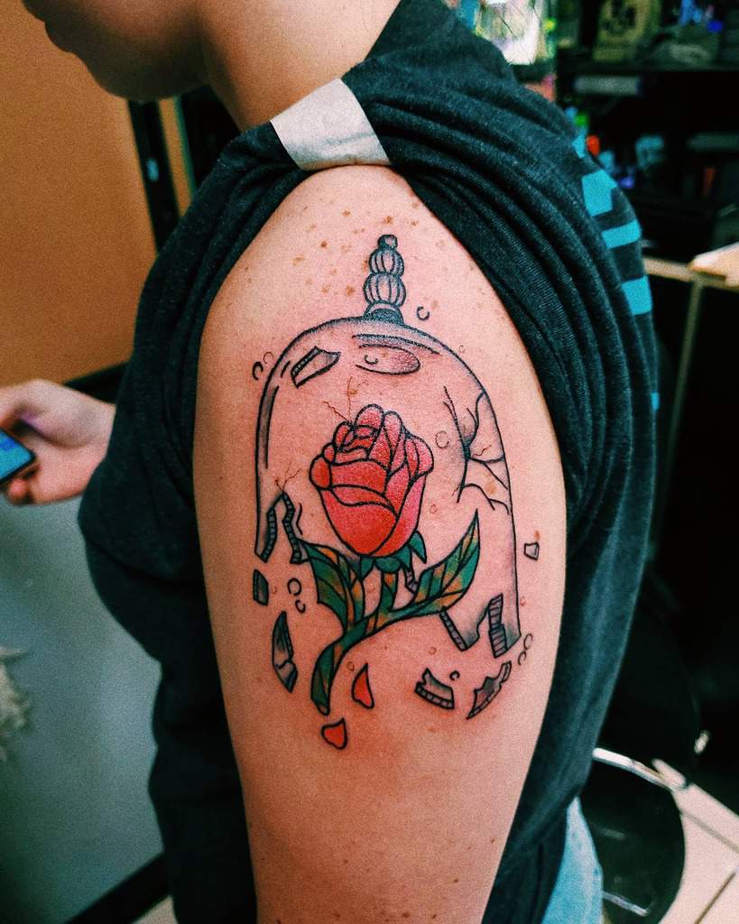 A colorful Beauty and the Beast rose tattoo with a shattered glass dome, featuring bold lines and vibrant red and green hues