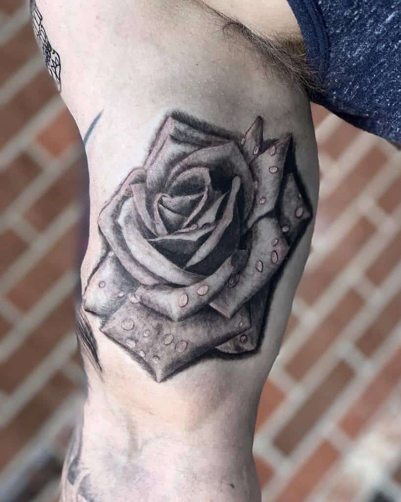 Realistic black and grey rose tattoo on the arm with detailed petals and water droplet effects for added depth
