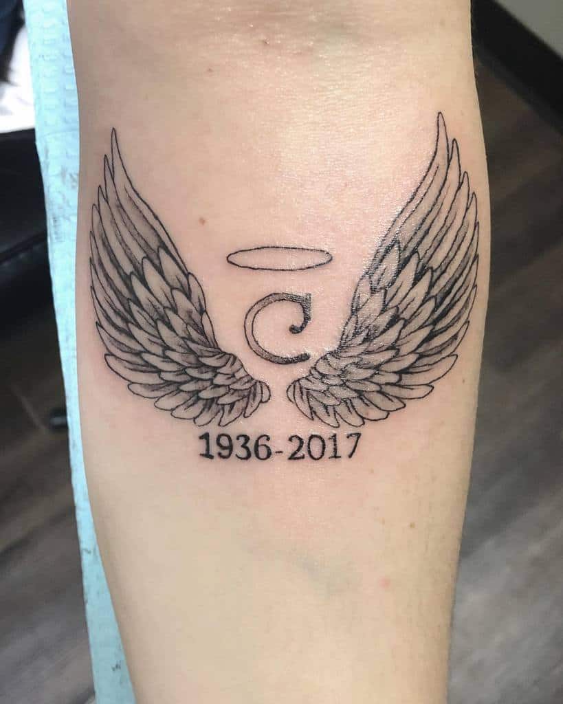Tattoo of angel wings around a letter 'C' and halo, with "1936-2017" below