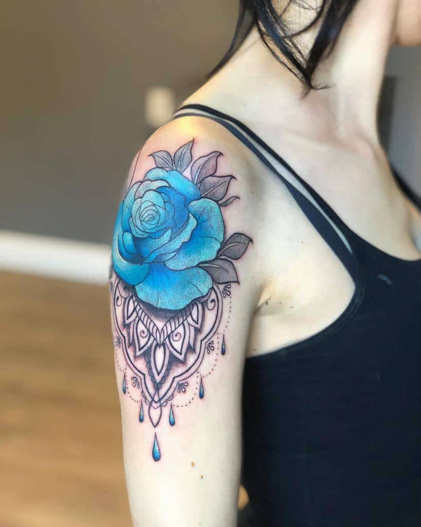 A vibrant blue rose tattoo with delicate mandala-style designs and water droplet accents, inked on the upper arm
