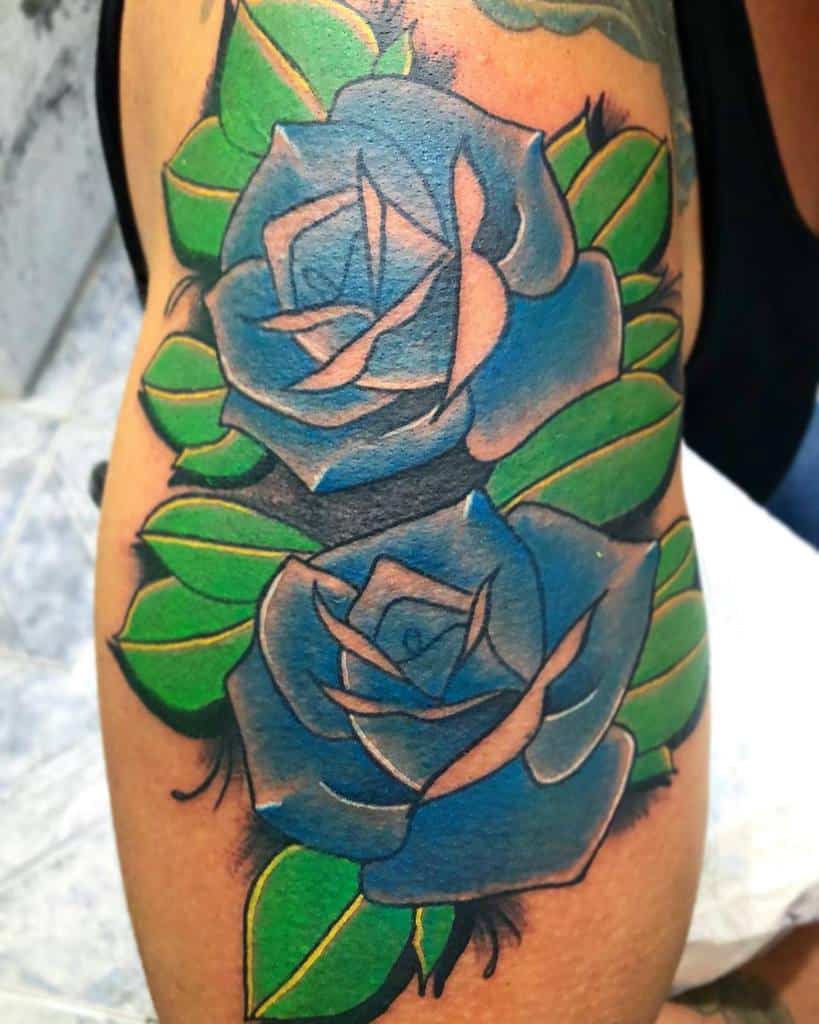 A stunning arm tattoo featuring a blue rose design, with two intertwined blossoms and lush green leaves