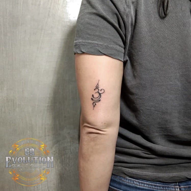 Small elegant tattoo on the upper arm featuring a stylized design of the Om symbol with delicate swirls