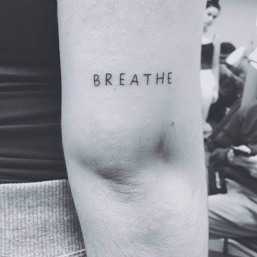 A forearm displays the word "BREATHE" elegantly tattooed in bold black ink, serving as a constant reminder to pause and embrace each moment