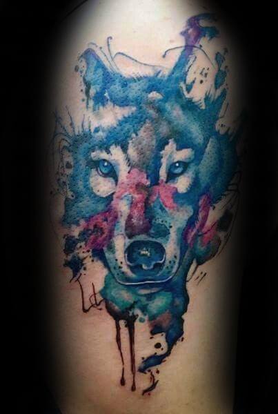 Watercolor wolf tattoo with intense blue and red splashes, dripping ink effect, and piercing eyes for a bold, artistic look.