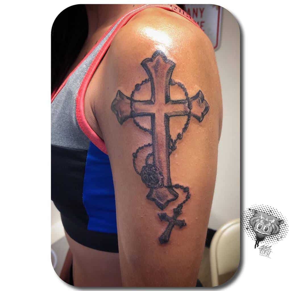 A striking tattoo of a cross intertwined with a rosary adorns the woman's upper arm