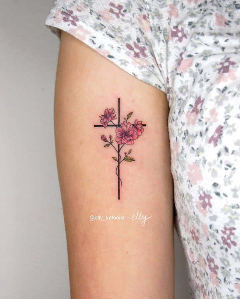 A tattoo of a cross gracefully entwined with pink flowers and green leaves adorns the upper arm