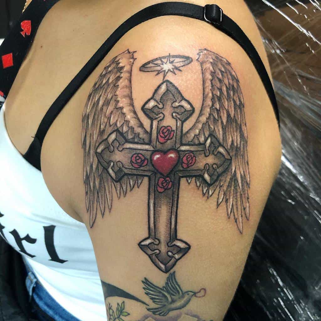 A stunning tattoo of a cross with wings, adorned by roses, a halo, and a heart graces the upper arm