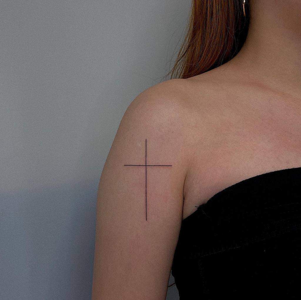 A woman with a subtly elegant cross tattoo graces her upper arm