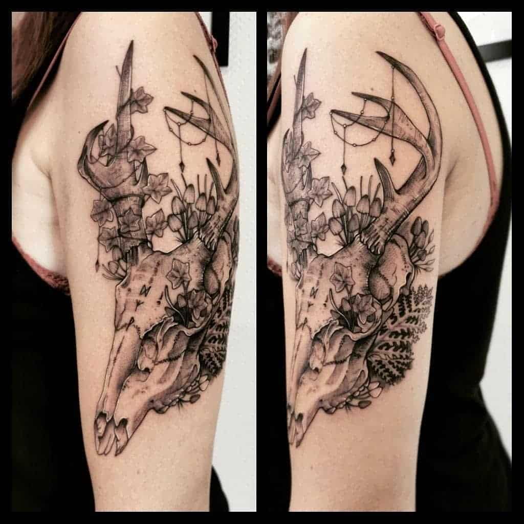 An arm tattoo featuring a striking deer skull with antlers, intricately adorned with flowers and foliage