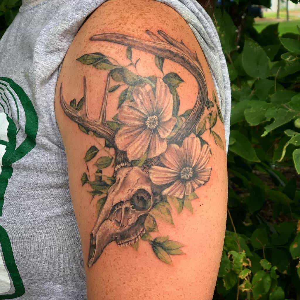 Arm tattoo of a deer skull with antlers entwined with flowers and leaves