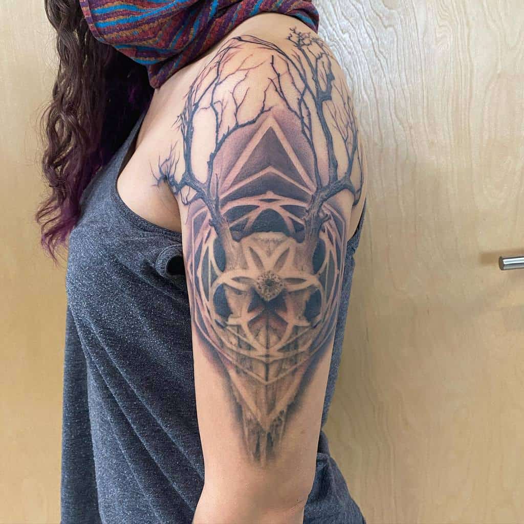 Woman with a detailed tattoo of geometric shapes, tree branches, and a deer skull on the upper arm