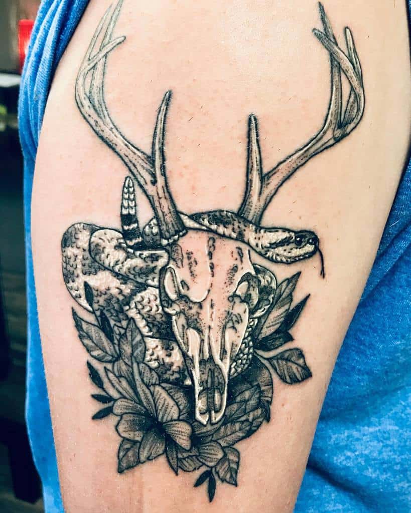 Tattoo of a deer skull with prominent antlers and a coiled snake on an upper arm