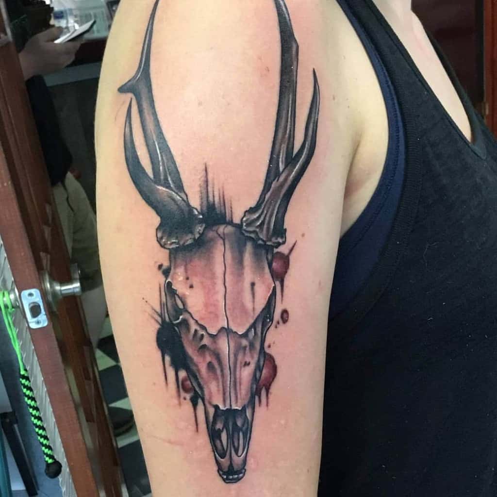 Forearm tattoo of a deer skull with antlers, featuring intricate shading and vibrant splash effects