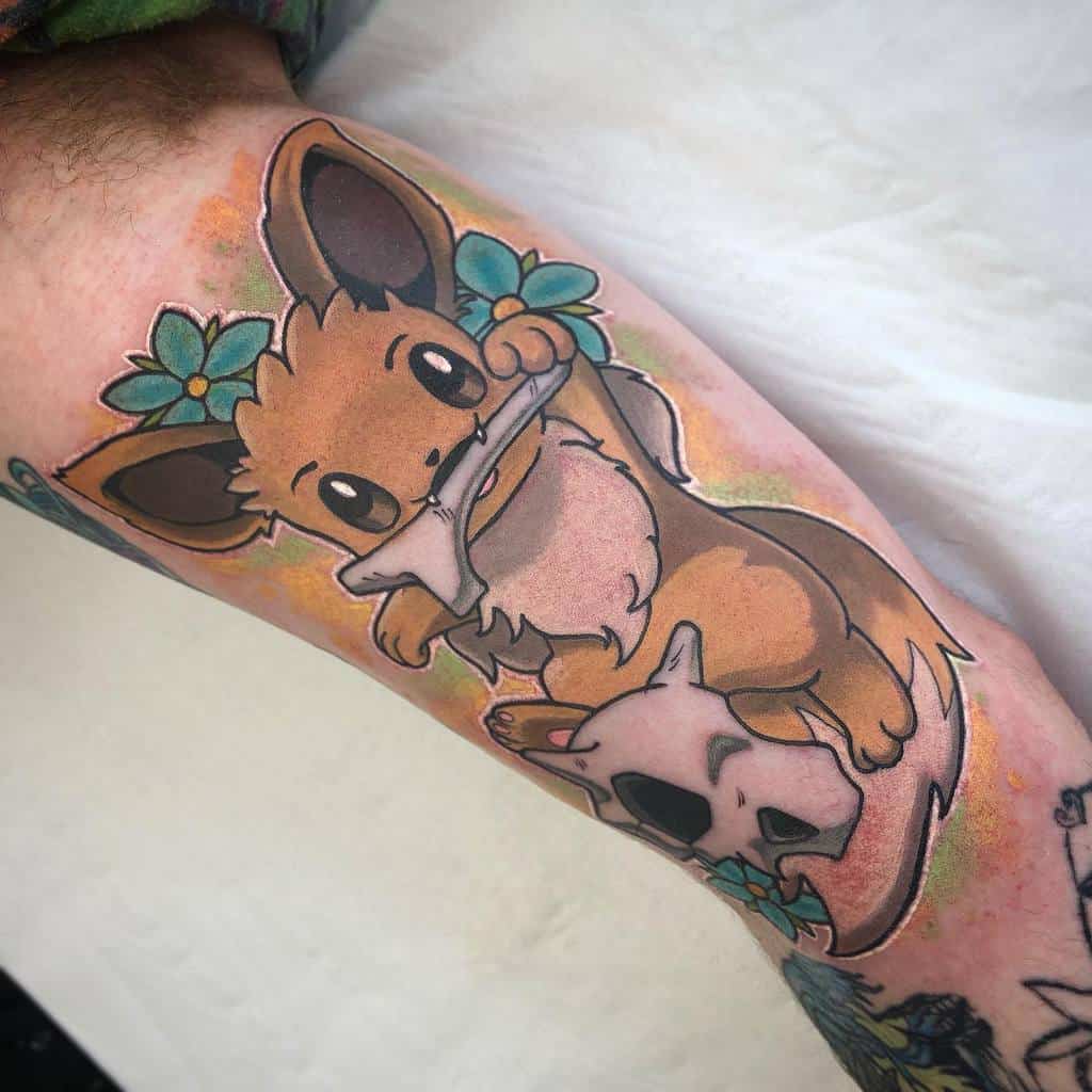 Vibrant Eevee tattoo with floral accents, playfully holding a skull, blending cute and edgy elements in a colorful design