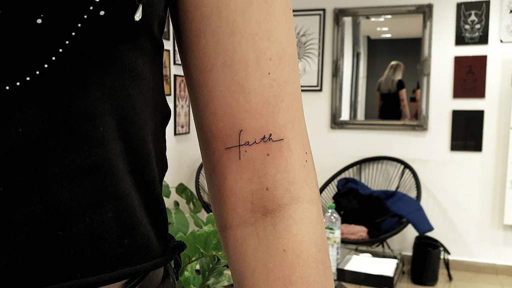 A tattoo of the word "faith" elegantly graces an upper arm