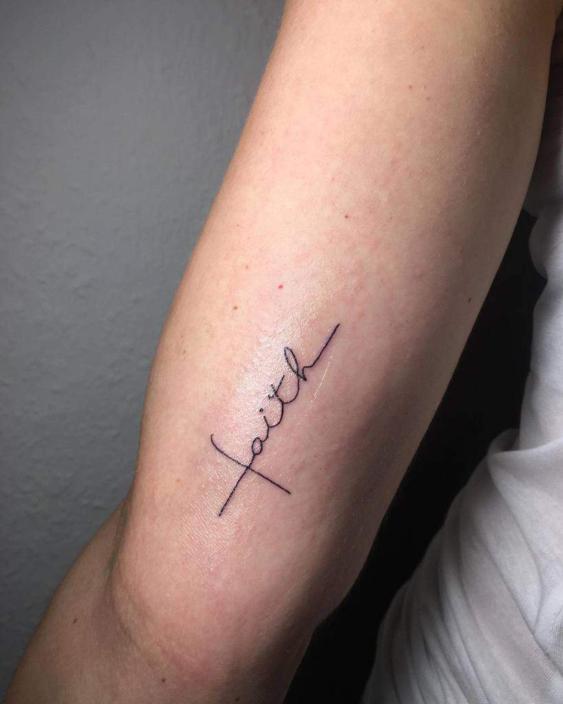 Minimalist "faith" tattoo on an inner arm in cursive script, elegantly enhanced with a delicate cross