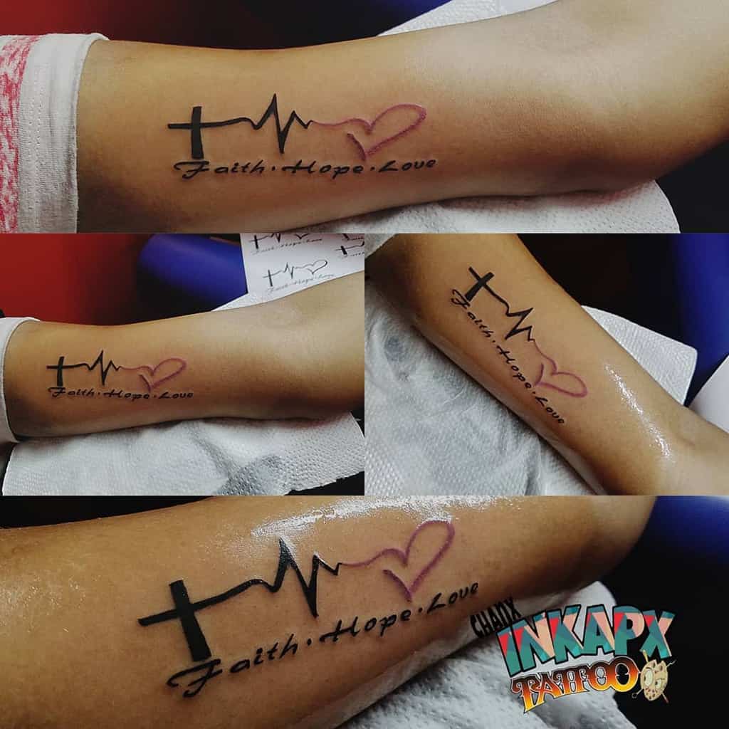 Arm tattoo featuring the words 'Faith, Hope, Love' with a cross, heartbeat line, and heart symbol, blending spiritual and emotional symbols in a minimalist design