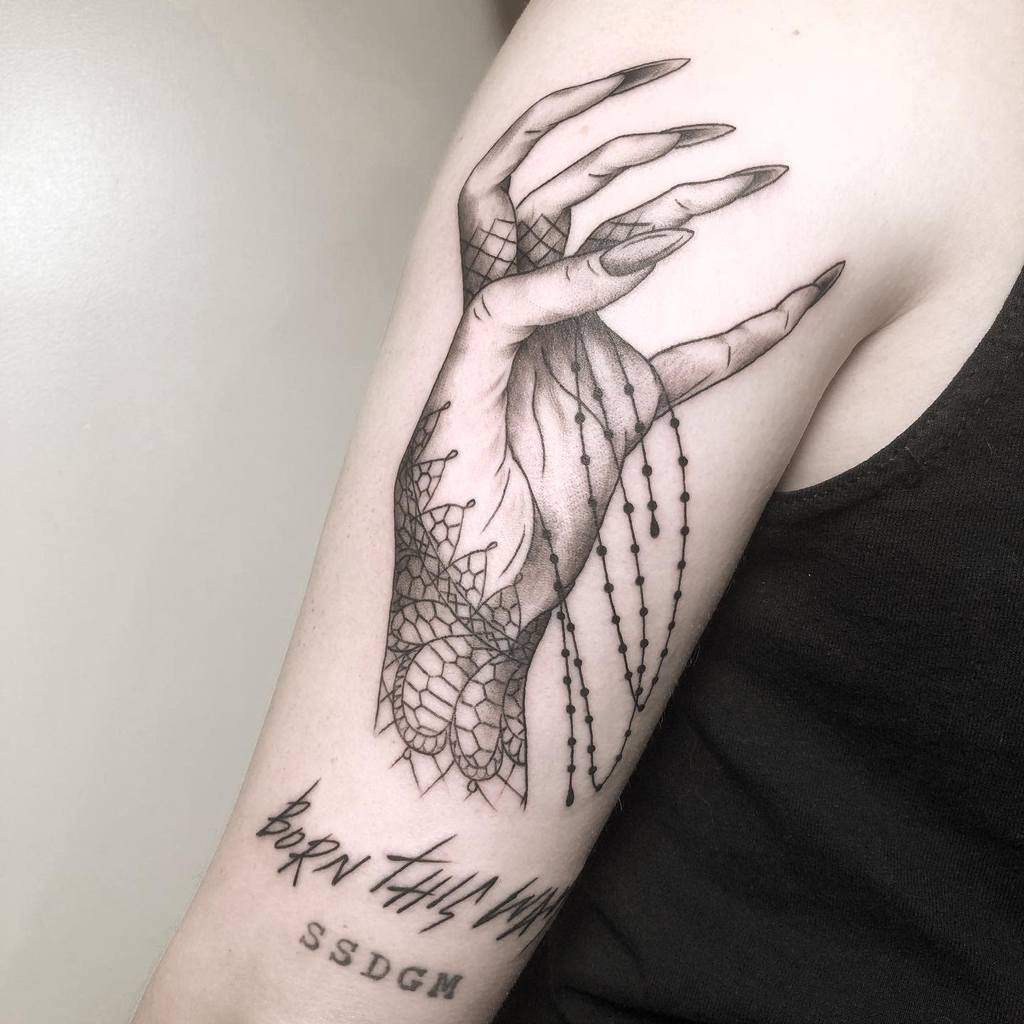 Tattoo of a hand with lace and beads on an arm with the text "BORN THIS WAY" and "SSDGM"