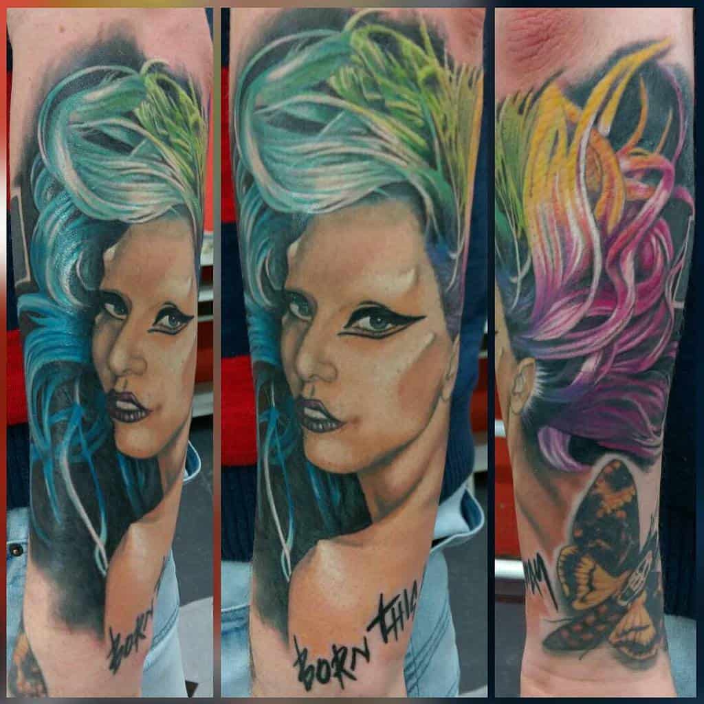 Colorful tattoo featuring Lady Gaga's portrait with vibrant hair, bold eyeliner, 'Born This Way' text, and a detailed butterfly design
