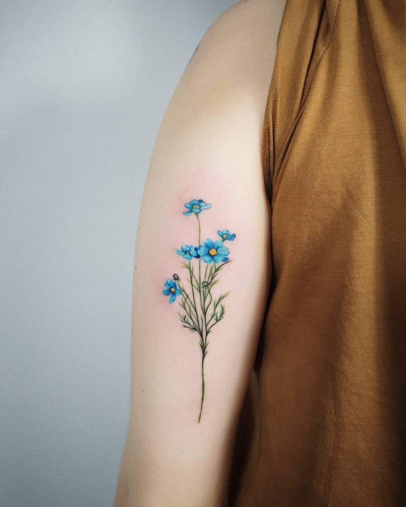 A forget me not blue flower tattoo graces a person's upper arm