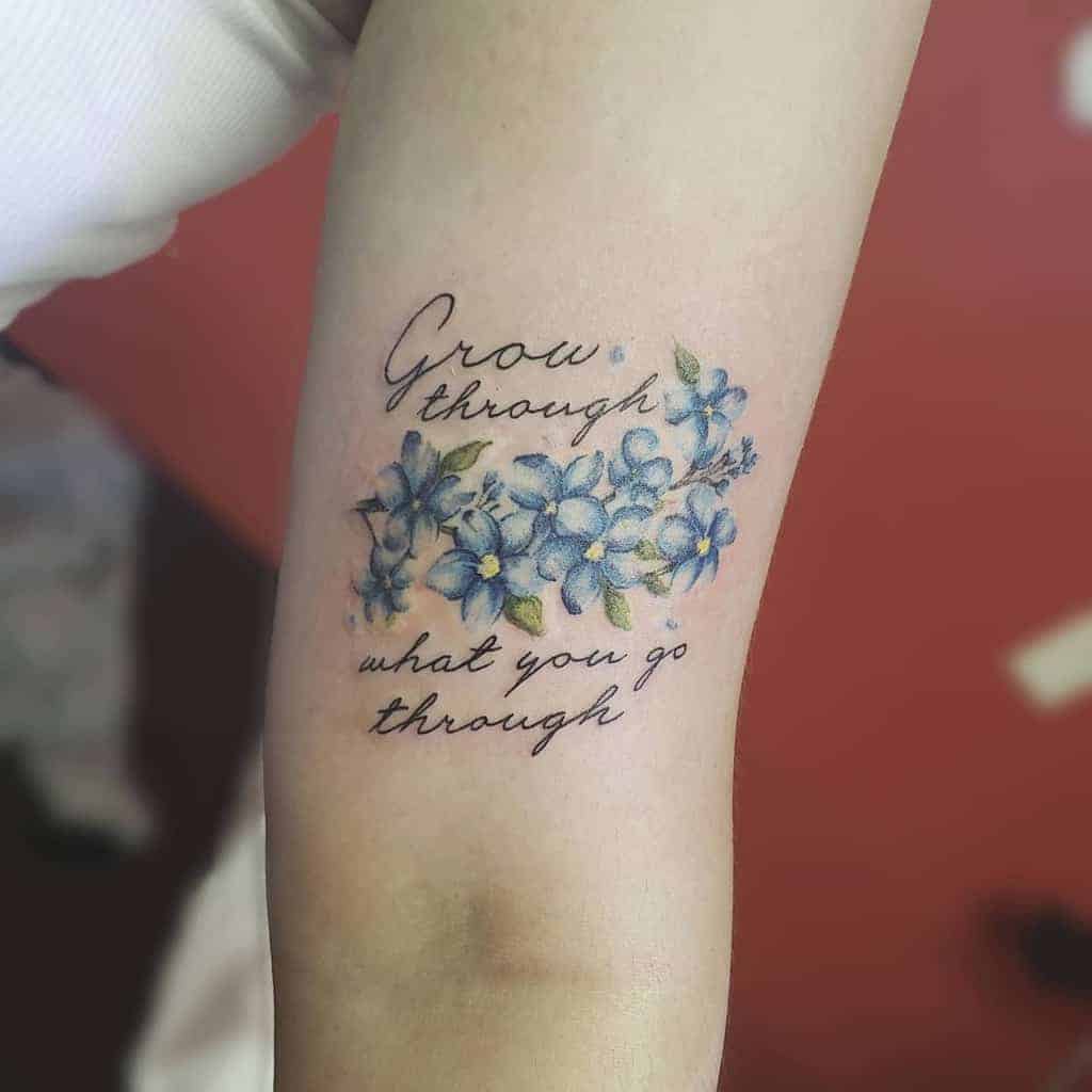 Arm tattoo beautifully combines delicate forget-me-not flowers with the motivational quote, "Grow through what you go through"
