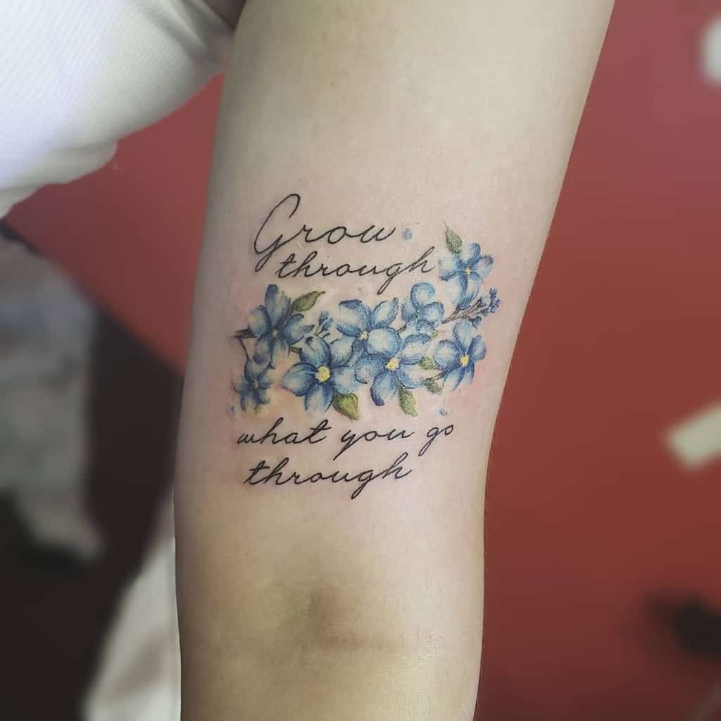 Tattoo of delicate forget-me-nots intertwined with the words "Grow through what you go through" elegantly inked on an arm