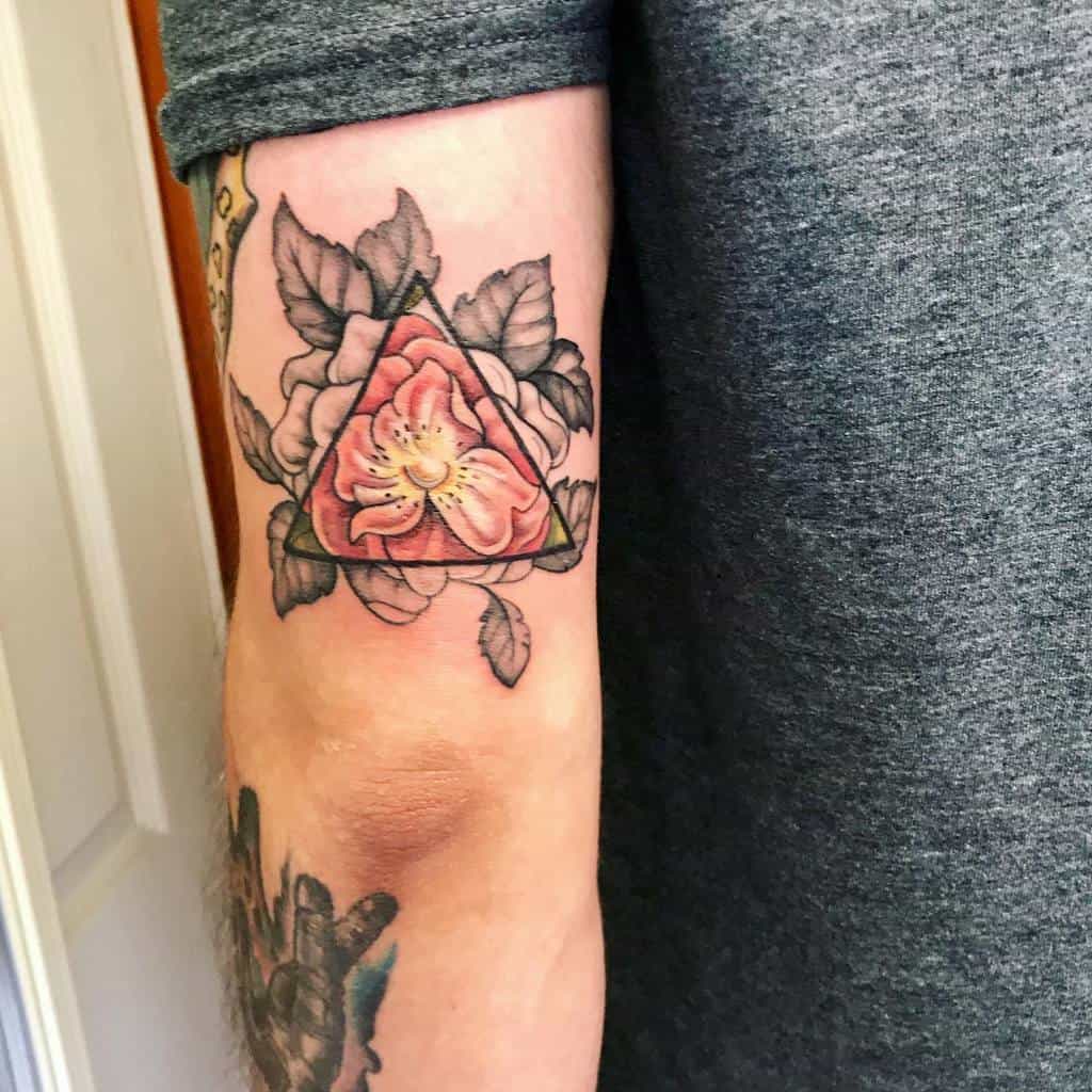 Floral tattoo on a person's arm, featuring a rose within a triangle, surrounded by detailed leaves
