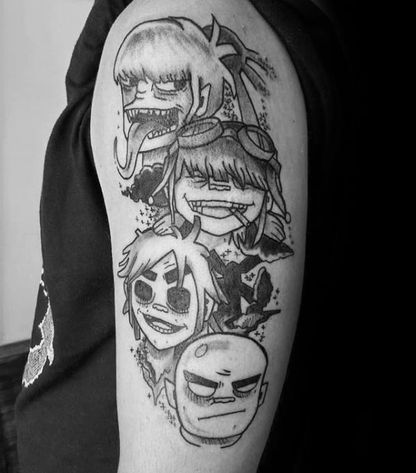 Black and grey upper arm tattoo featuring all four Gorillaz band members in a bold, sketchy style with ink splatter effects.