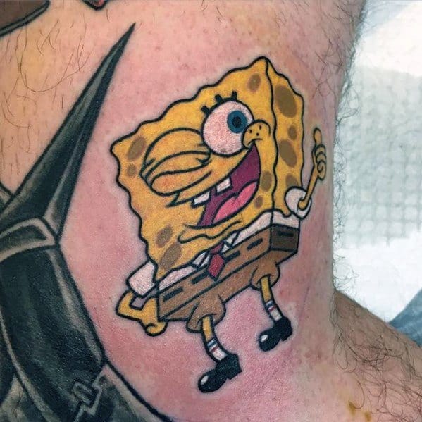 Playful SpongeBob tattoo with one eye winking, wide smile, and thumb up, showcasing his cheerful personality on skin.