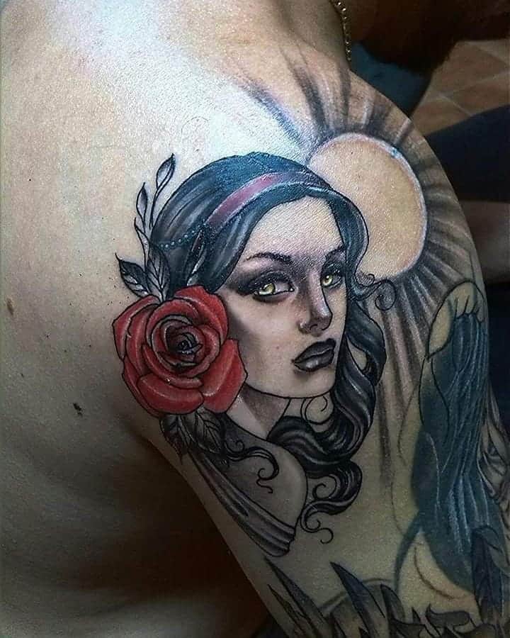 A shoulder tattoo depicting a gypsy woman with flowing black hair, a vibrant red rose, and a radiant sun in the background