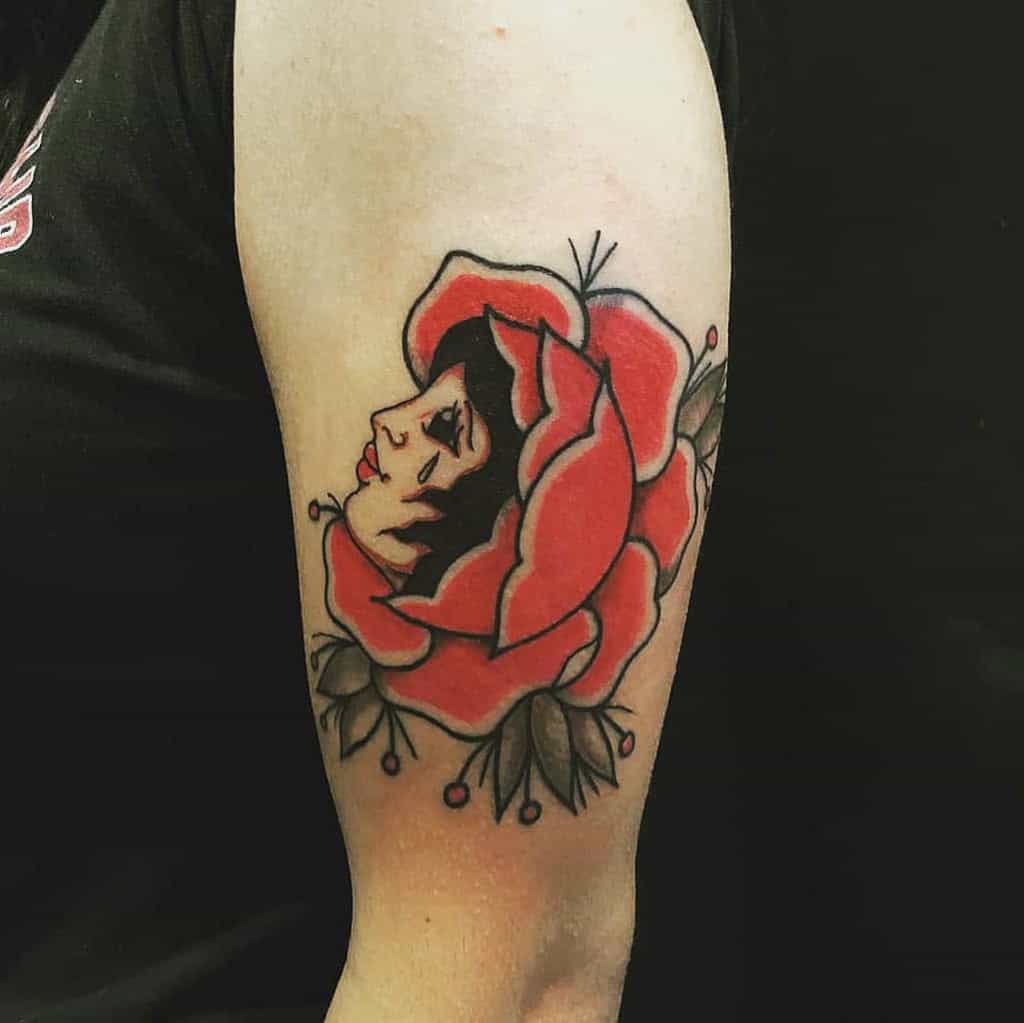 Tattoo of a gypsy woman's face nestled within a large red rose with green leaves on an arm