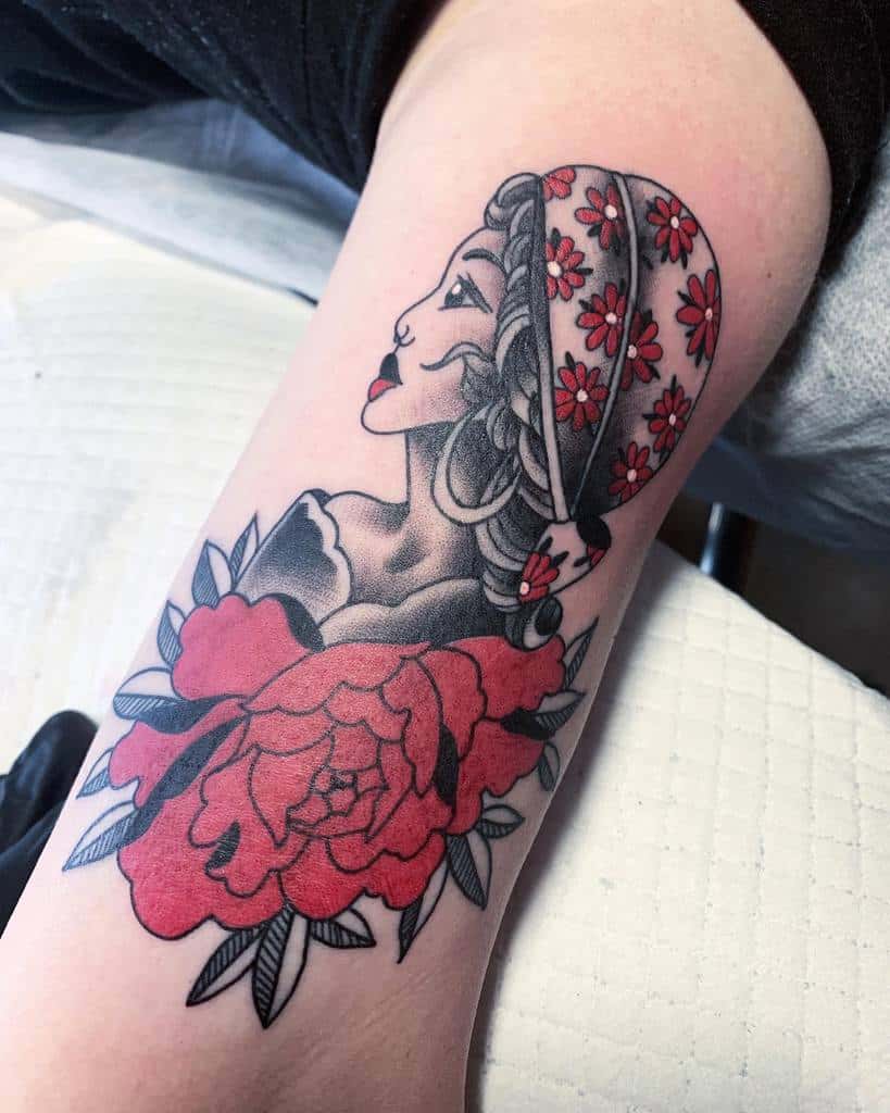 A tattoo featuring a gypsy woman's profile, adorned with a floral headscarf and surrounded by vibrant red flowers