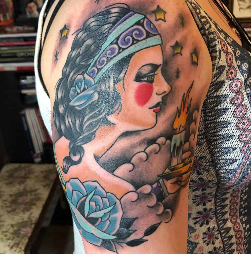 Tattoo of a gypsy woman with a candle, stars, and flowers on an upper arm