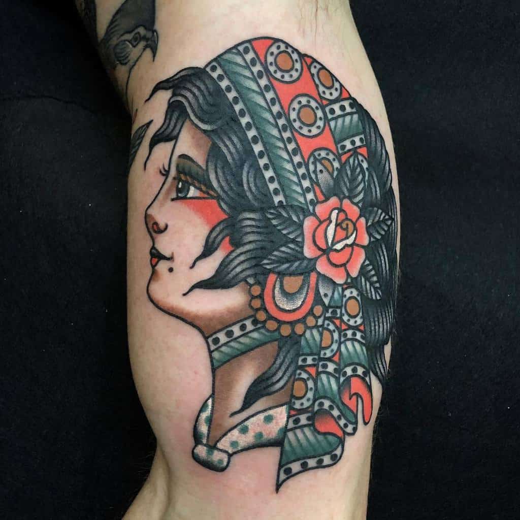 Tattoo of a gypsy woman's profile adorned with a floral headscarf and intricate patterns on an arm
