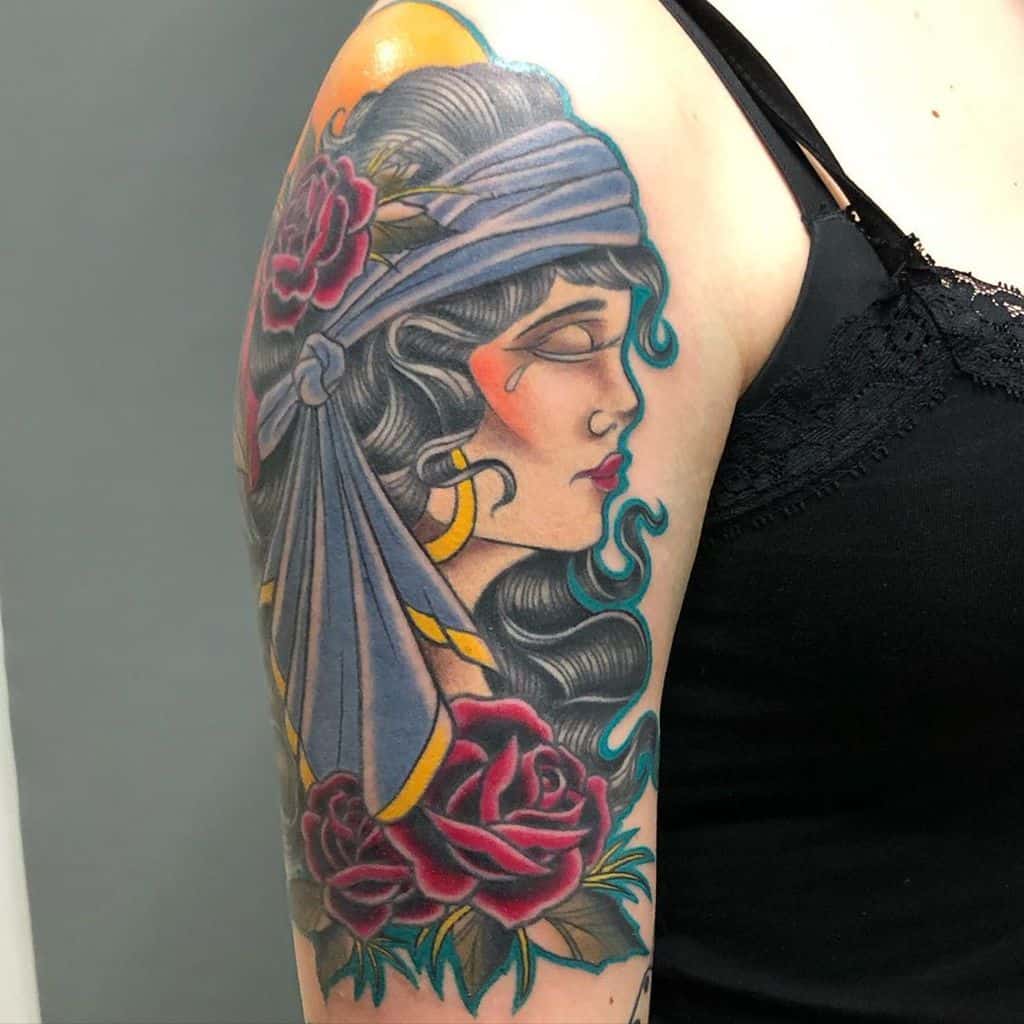 Tattoo of a gypsy woman with roses and a headscarf on an upper arm