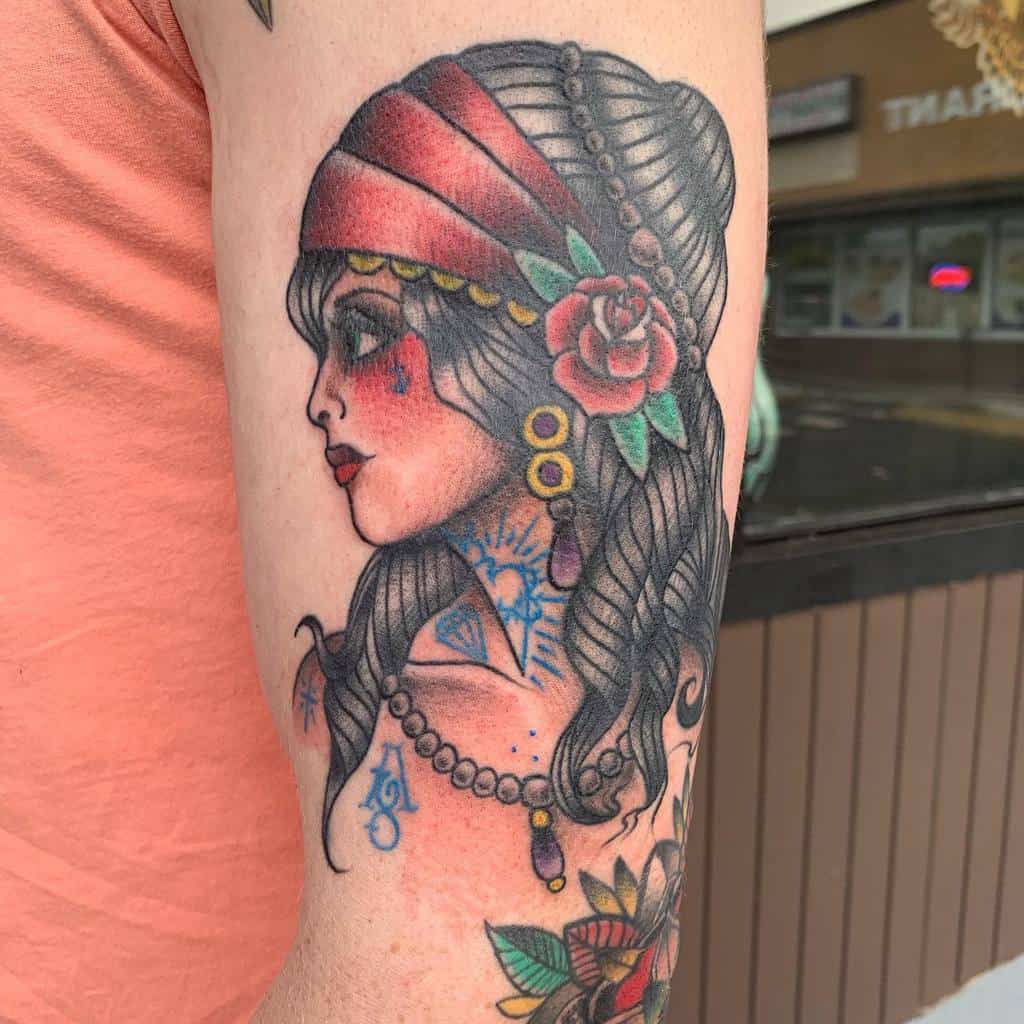 Tattoo of a gypsy woman adorned with a red headscarf and rose, vintage style, on an upper arm