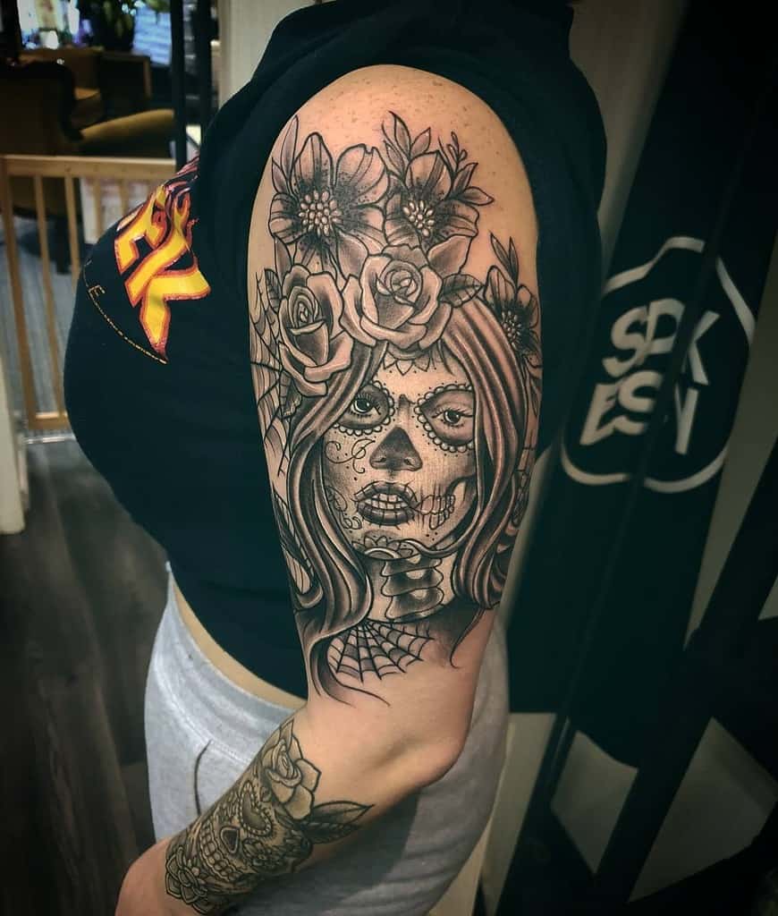 A vibrant tattoo of a Day of the Dead skull woman, with intricate floral designs, adorns the arm like a mystical gypsy's charm