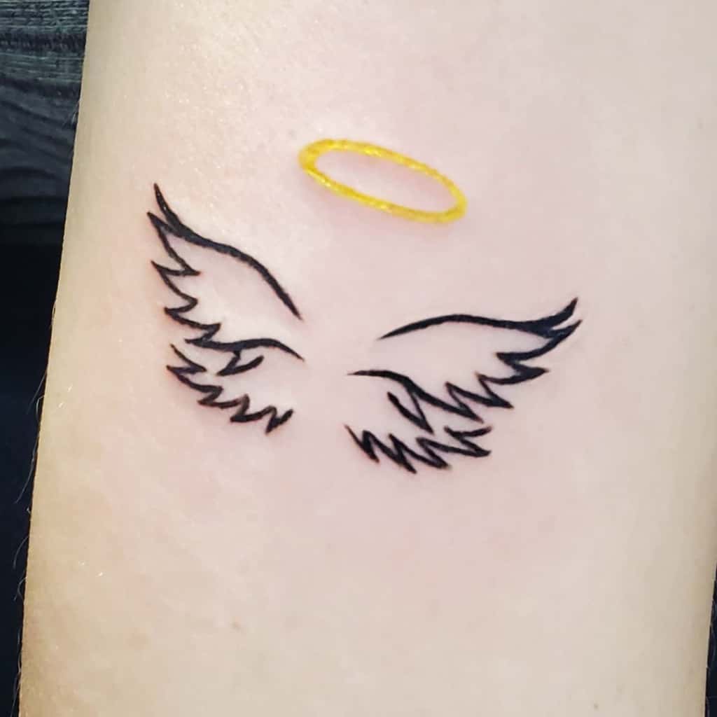 Tattoo of stylized black angel wings with a small golden halo above