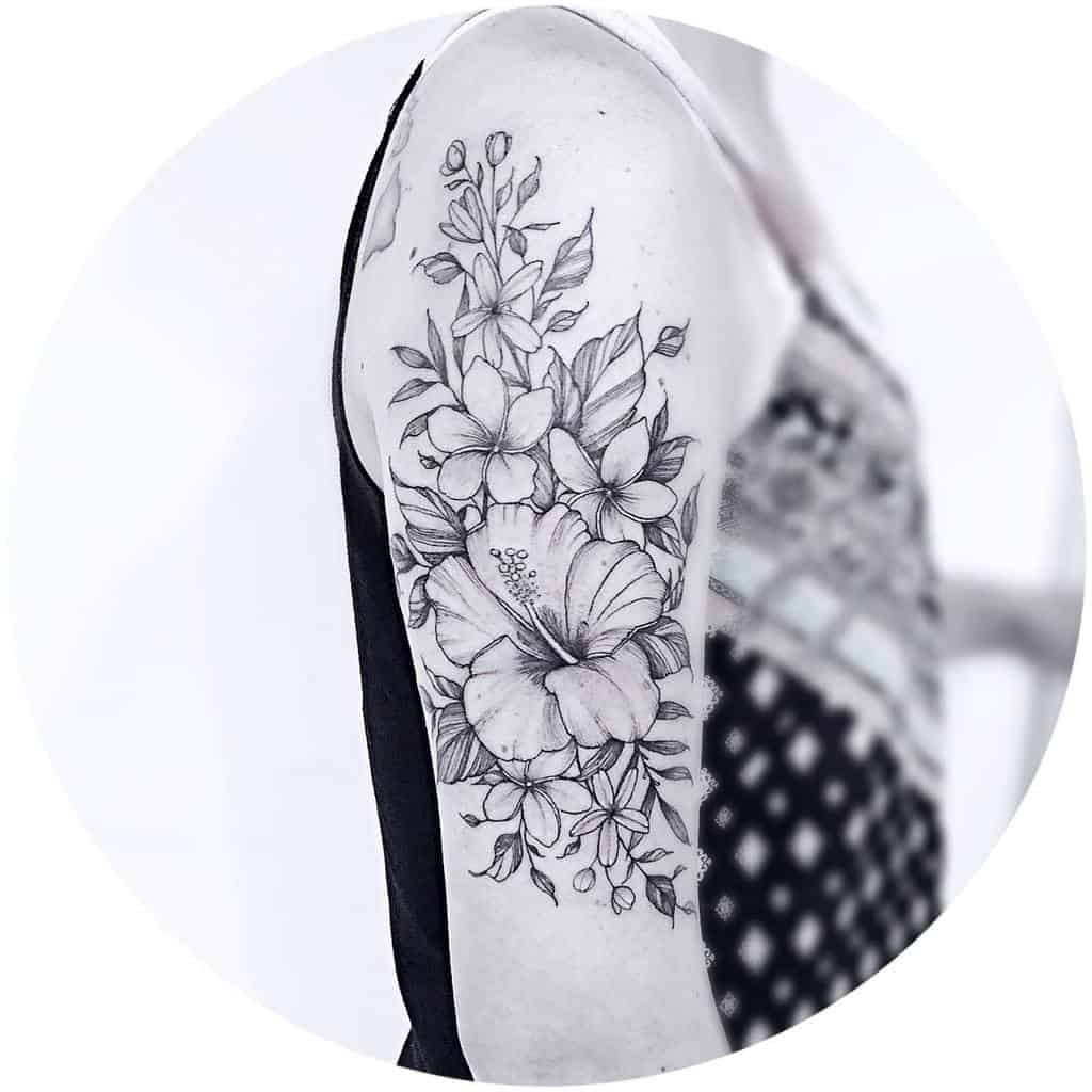 Black and grey upper arm tattoo featuring detailed hibiscus and plumeria flowers with delicate leaves