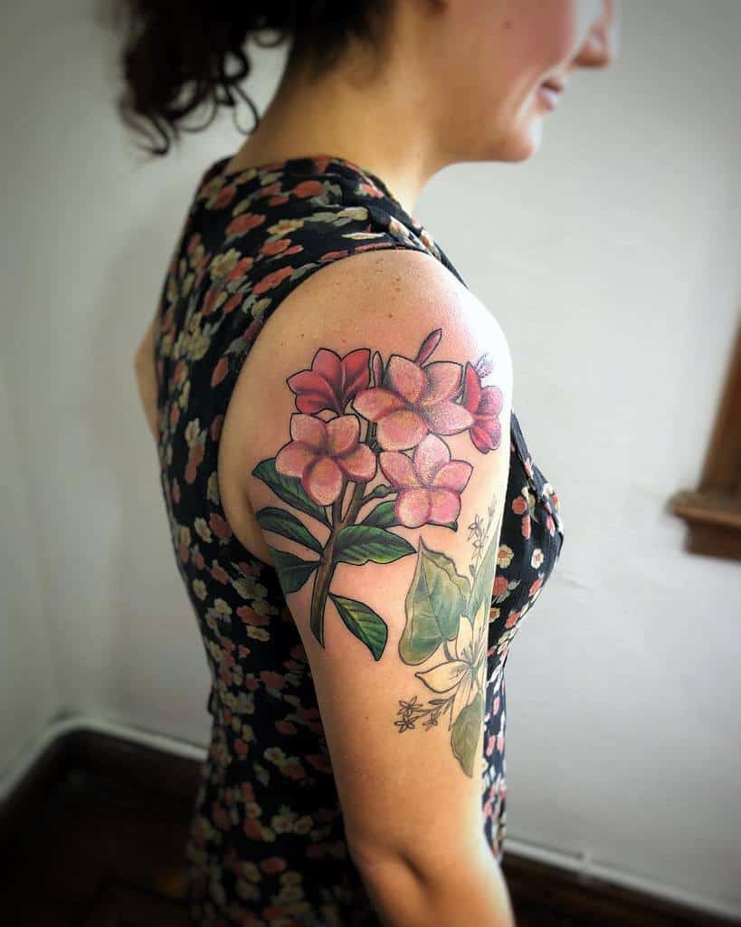 Upper arm tattoo featuring pink plumeria flowers with vibrant green leaves, showcasing a natural and tropical design