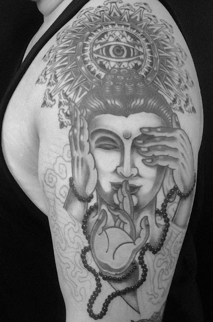 Intricate arm tattoo of a Buddha face with hands symbolizing 'Hear No Evil, See No Evil, Speak No Evil,' adorned with an all-seeing eye and prayer beads