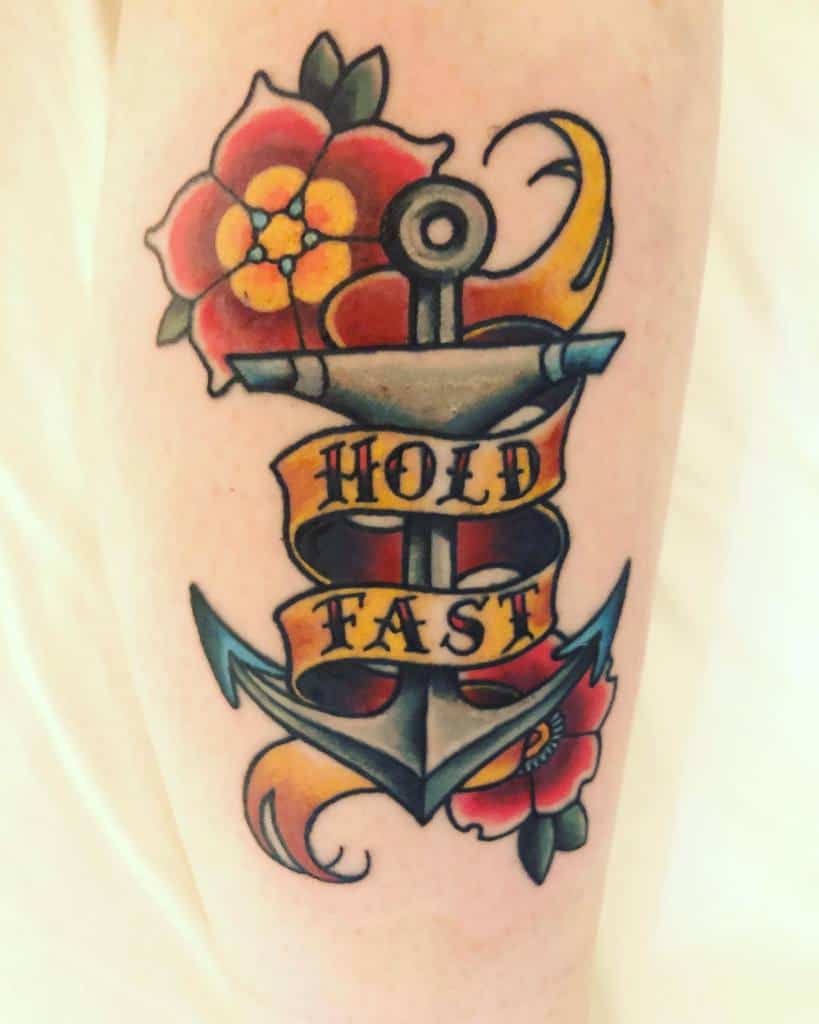 Tattoo of an anchor with flowers and a banner reading "Hold Fast"