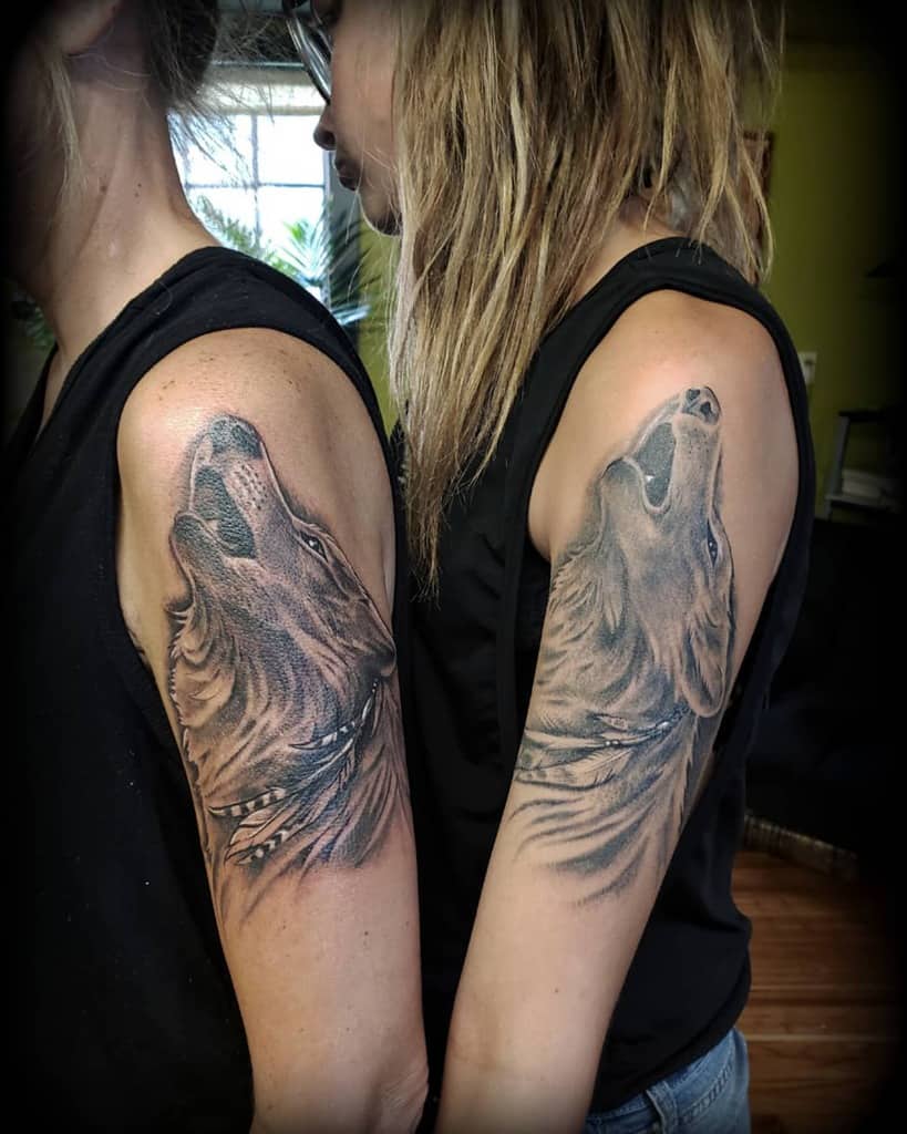 Two people, each with a brilliantly crafted wolf tattoo on their upper arms, stand back to back, showcasing their bond