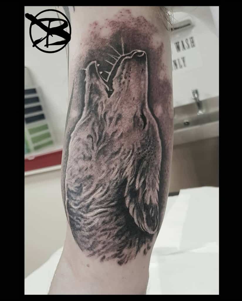 A striking black and gray tattoo of a majestic wolf howling adorns the forearm